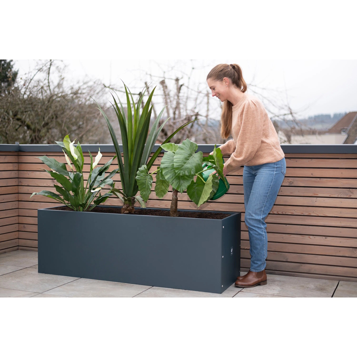 Herstera Garden Pflanzkasten, anthrazit, 150x50x50 cm, mit Pflanzen und Frau beim Gießen.