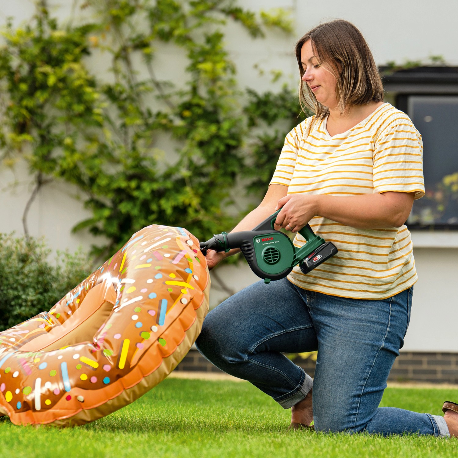 Frau pumpt Donut-Luftmatratze mit Bosch Akku-Laubbläser UniversalLeafBlow auf.