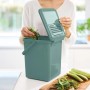 Grüner PROREGAL Abfalleimer mit Deckel und Kohlefilter, 9 Liter. Frau befüllt den Mülleimer mit Gemüseresten.