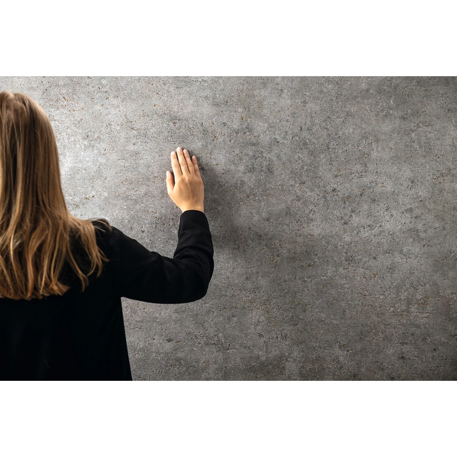 Egger DecoWall Wandpaneel Rovigo Beton, graue Betonoptik, Frau berührt die Paneele.