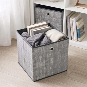 Hellgraue Stoff-Aufbewahrungsbox mit Metallgriff, gefüllt mit Kleidung und Büchern, vor einem Regal.