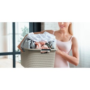 Frau trägt Rotho Wäschekorb Country 40 l Cappuccino, Rattan-Optik, gefüllt mit Wäsche.
