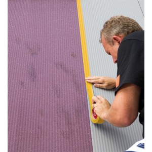 Mann klebt oranges Kip Washi-Tec Malerkreppband auf eine Wand. Klebeband 30 mm x 50 m.