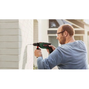 Mann bohrt mit Bosch UniversalImpact 800 Schlagbohrmaschine in Ziegelwand. Grüne Bohrmaschine mit 800 Watt für Heimwerker.