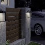 Schwarze Eglo Solar LED-Wandleuchte Suzzara mit Sensor an einer Hauswand und einem Zaun.