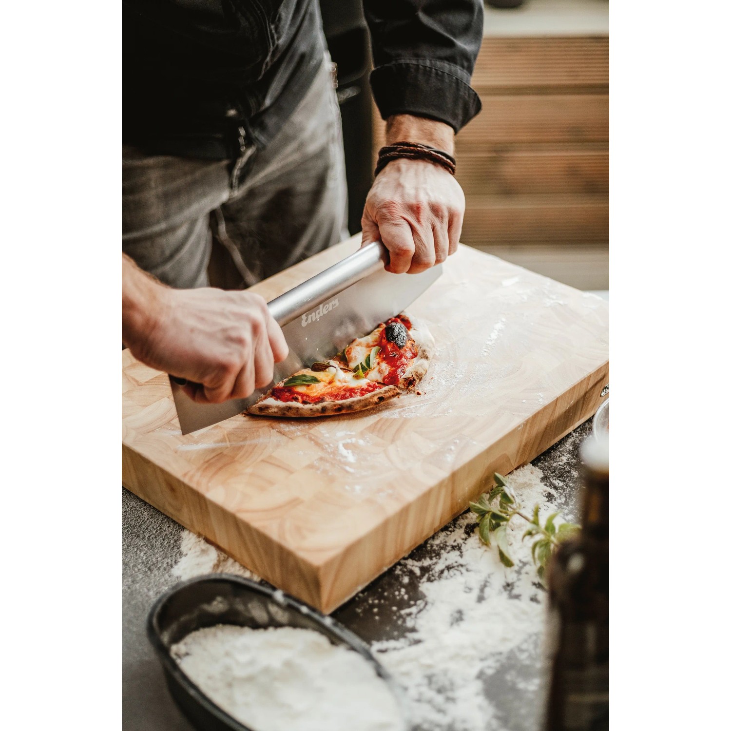 Enders Pizzaschneider aus Edelstahl schneidet Pizza auf Holzbrett. Grillutensil für präzise Pizzastücke.