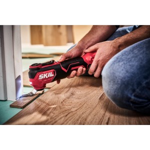 Skil Akku-Multifunktionswerkzeug beim Kürzen eines Laminatstücks. Das Werkzeug ist rot/schwarz und wird von einer Person bedient.