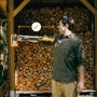 Mann mit Fiskars Spaltaxt X32 vor Holzstapel. Die Axt hat eine L-Klinge und ist 81,5 cm lang.