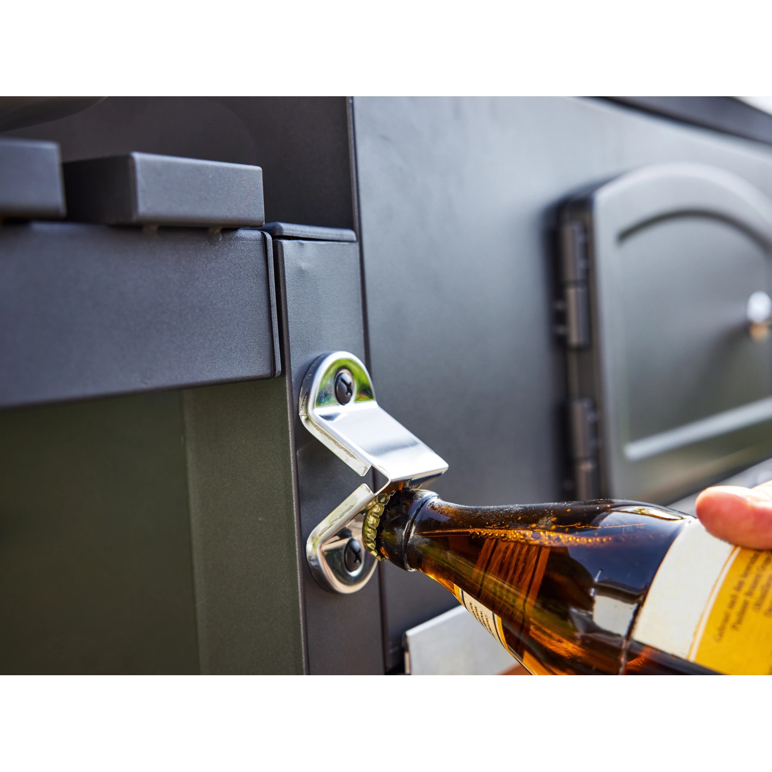 Flaschenöffner am Jamestown Holzkohlegrillwagen Jaxon XL beim Öffnen einer Bierflasche.