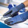 Hände mit LUX Schnittschutzhandschuhen (Größe 8) schneiden Papier mit einem Cutter.
