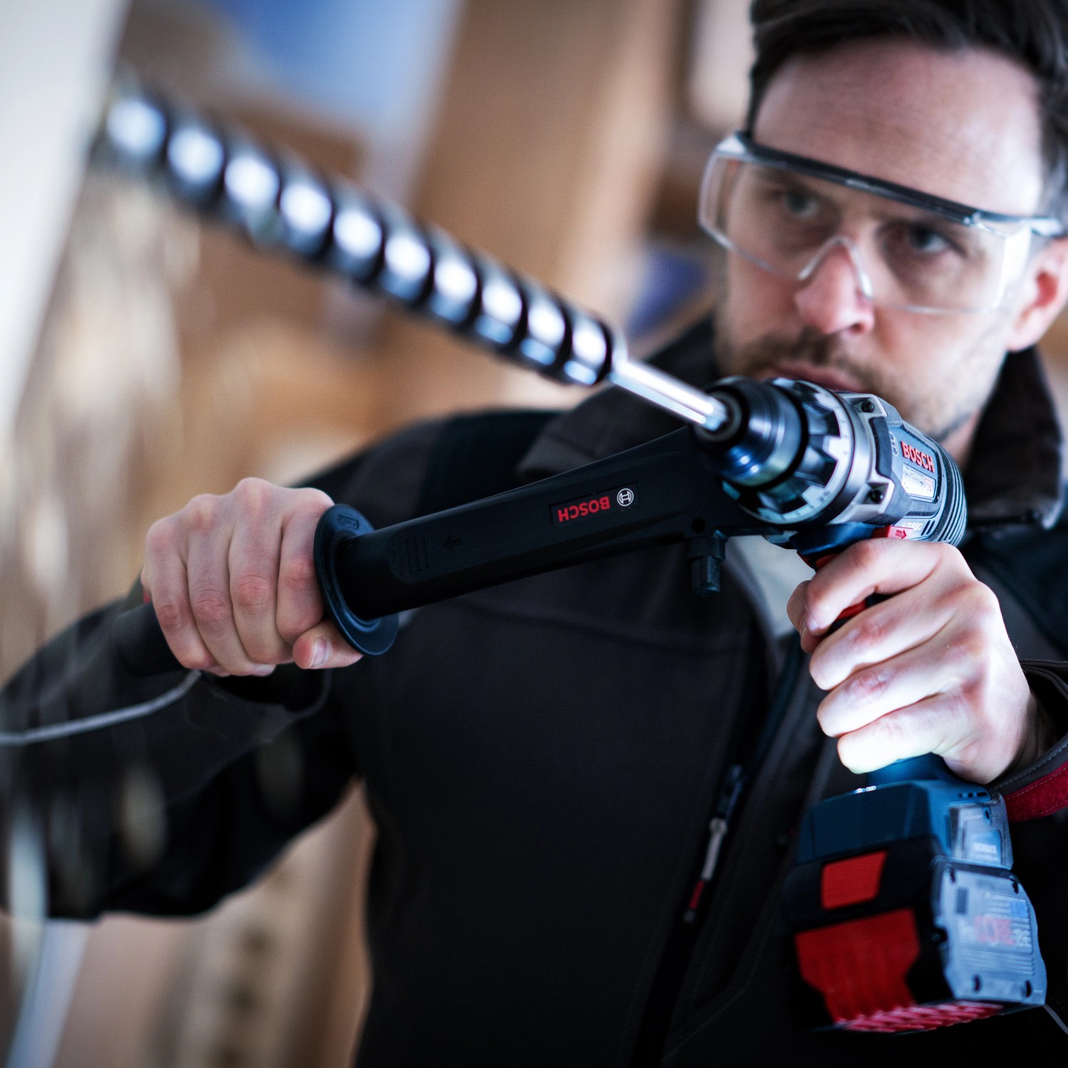 Mann bohrt mit Bosch Professional Akku-Bohrschrauber GSR 18V-150 C mit Zusatzhandgriff.