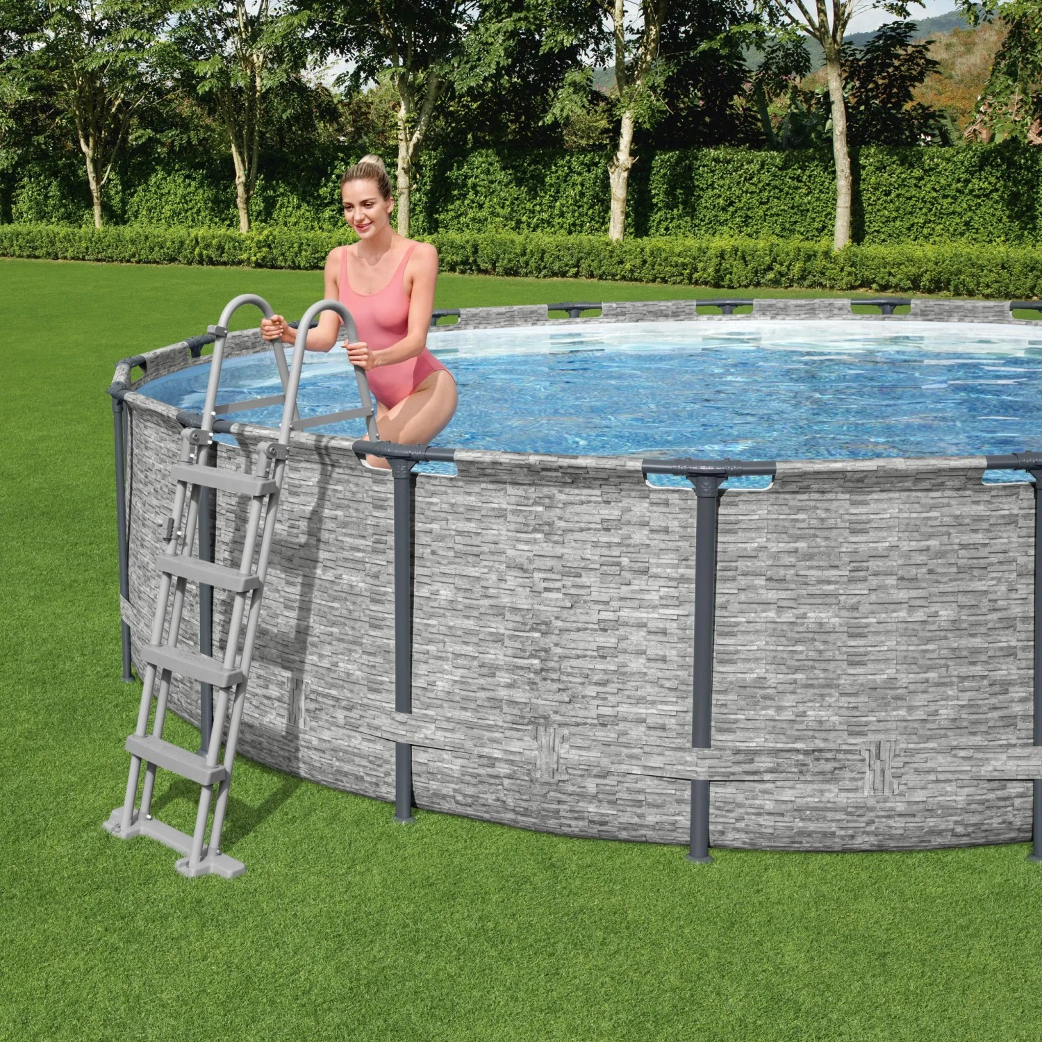 Bestway Stahlrahmenpool Set mit Leiter, Ø 427 cm, im Garten. Frau steigt über die Leiter in den Pool.