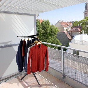 Klappbarer schwarz-grauer Bügelwäscheständer mit Kleidung auf Balkon. Ideal zum Trocknen von Hemden und Blusen.