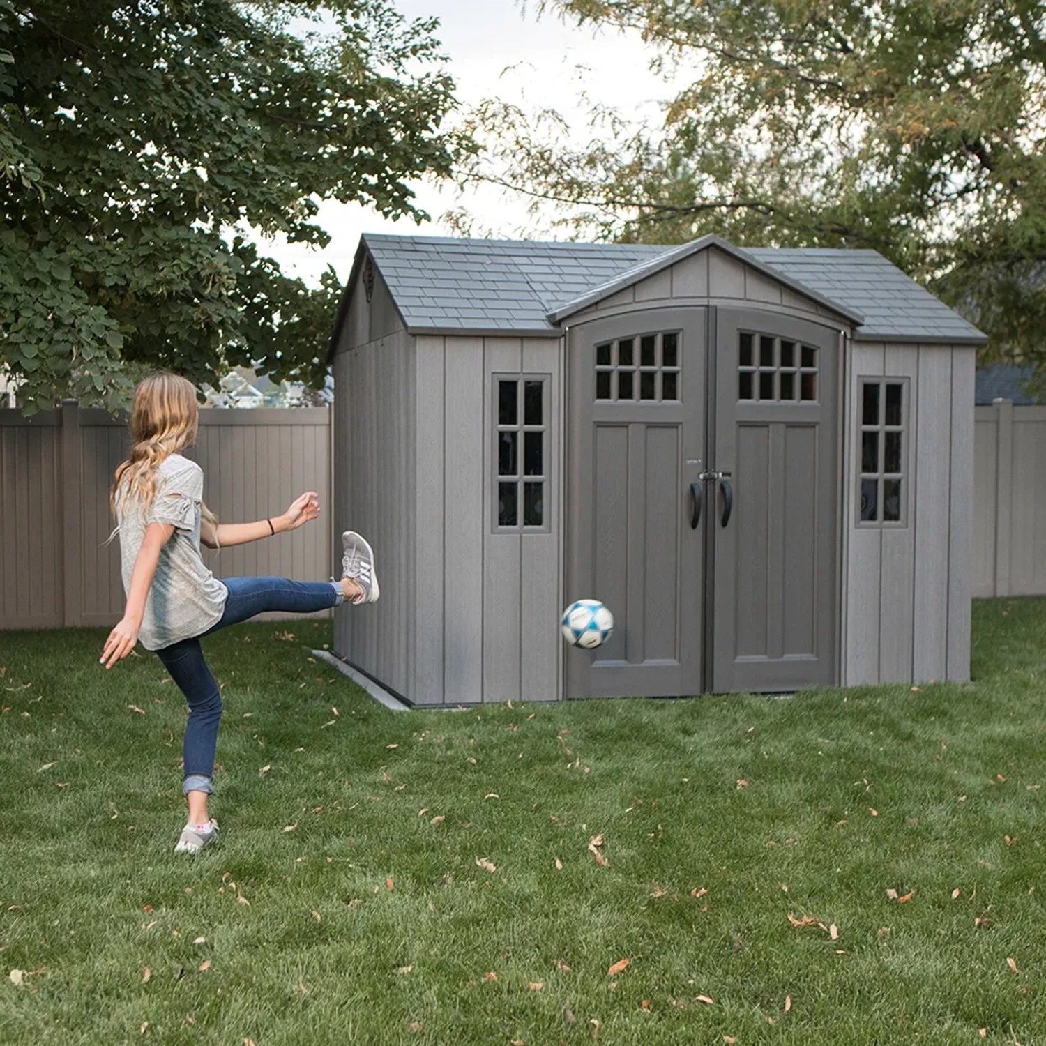 Graues Lifetime Kunststoff-Gartenhaus Saturn (6,6 m²) mit spielendem Kind im Garten.