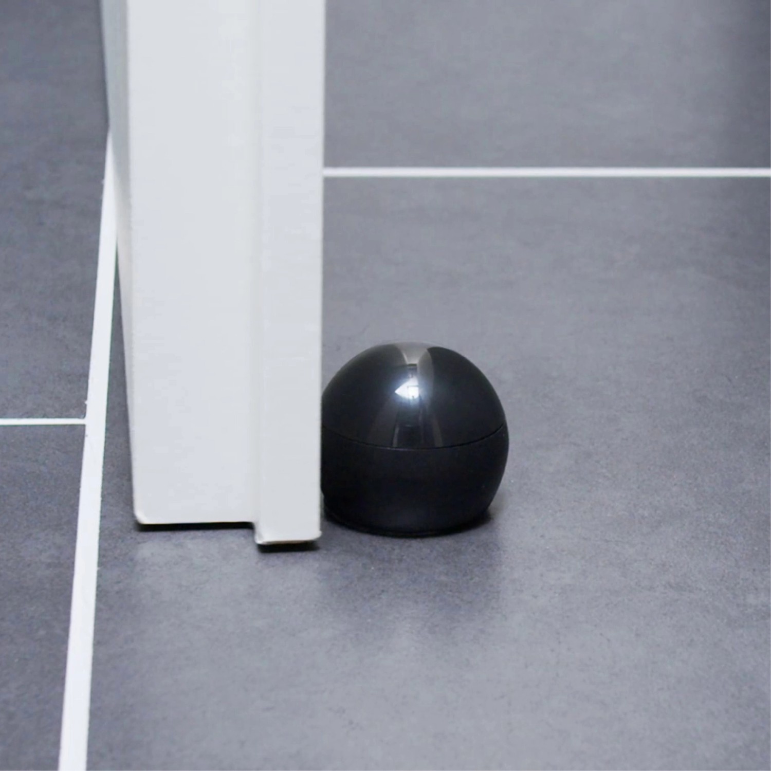 Schwarzer Wagner Bodentürstopper Black Deluxe (Ø 45 mm) am Türrahmen auf grauem Fliesenboden.