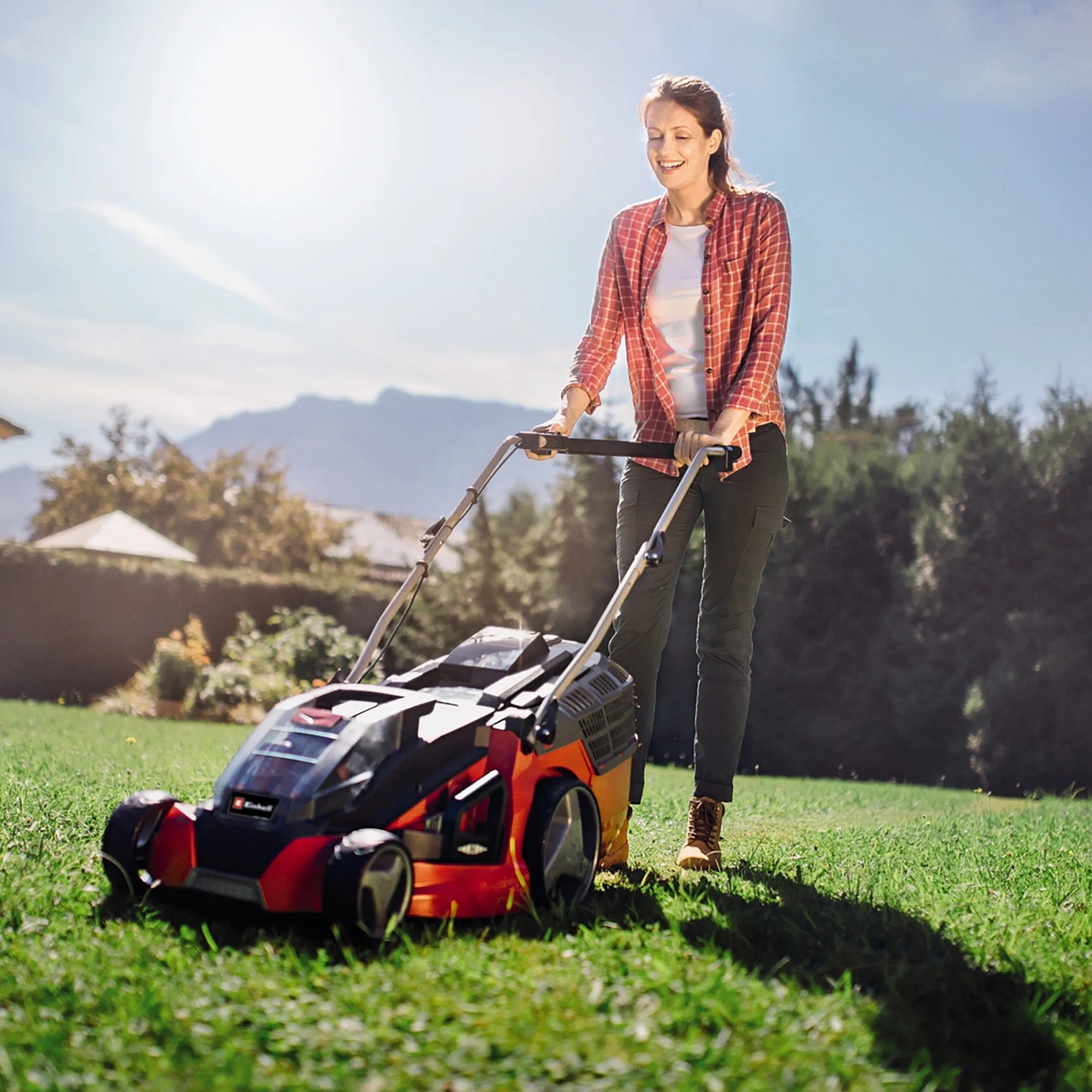 Frau bedient Einhell Akku-Rasenmäher GE-CM 43 Li im Garten. Inkl. 2 Akkus und 63 l Fangkorb.