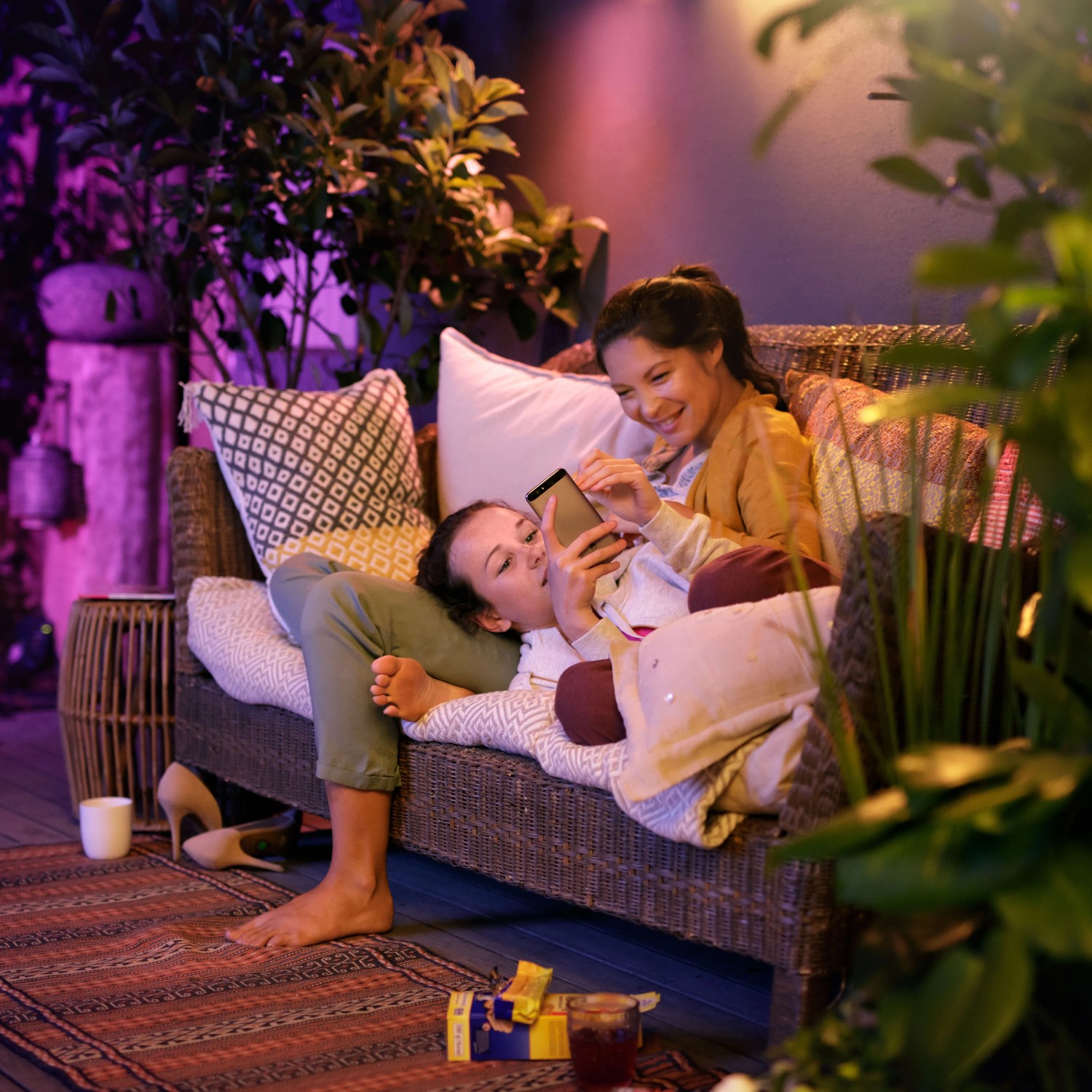 Philips Hue Calla Sockelleuchte, Erweiterung: Zwei Frauen entspannen im farbig beleuchteten Garten.