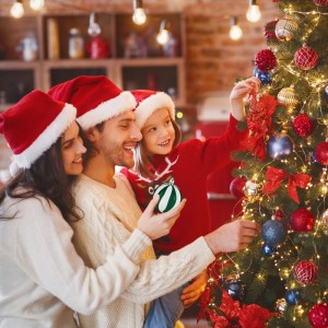 Familie schmückt festlich beleuchteten Tannenbaum mit bunten Weihnachtskugeln in matt, glänzend, glitzernd.