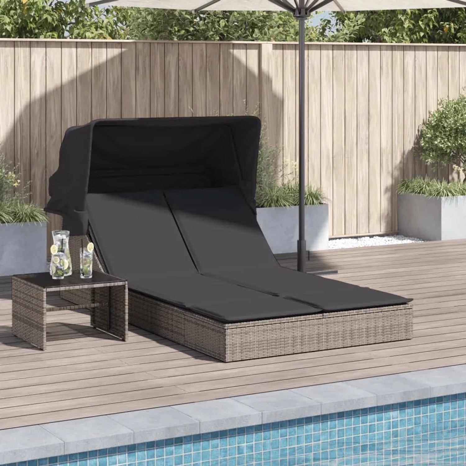 Graue Doppel-Sonnenliege mit Dach und Auflagen aus Poly Rattan neben Pool.