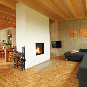Anthrazitfarbenes Relaxdays Kaminholzregal aus Stahl mit 2 Ablagen, gefüllt mit Holzscheiten, neben Kamin. Kaminzubehör.