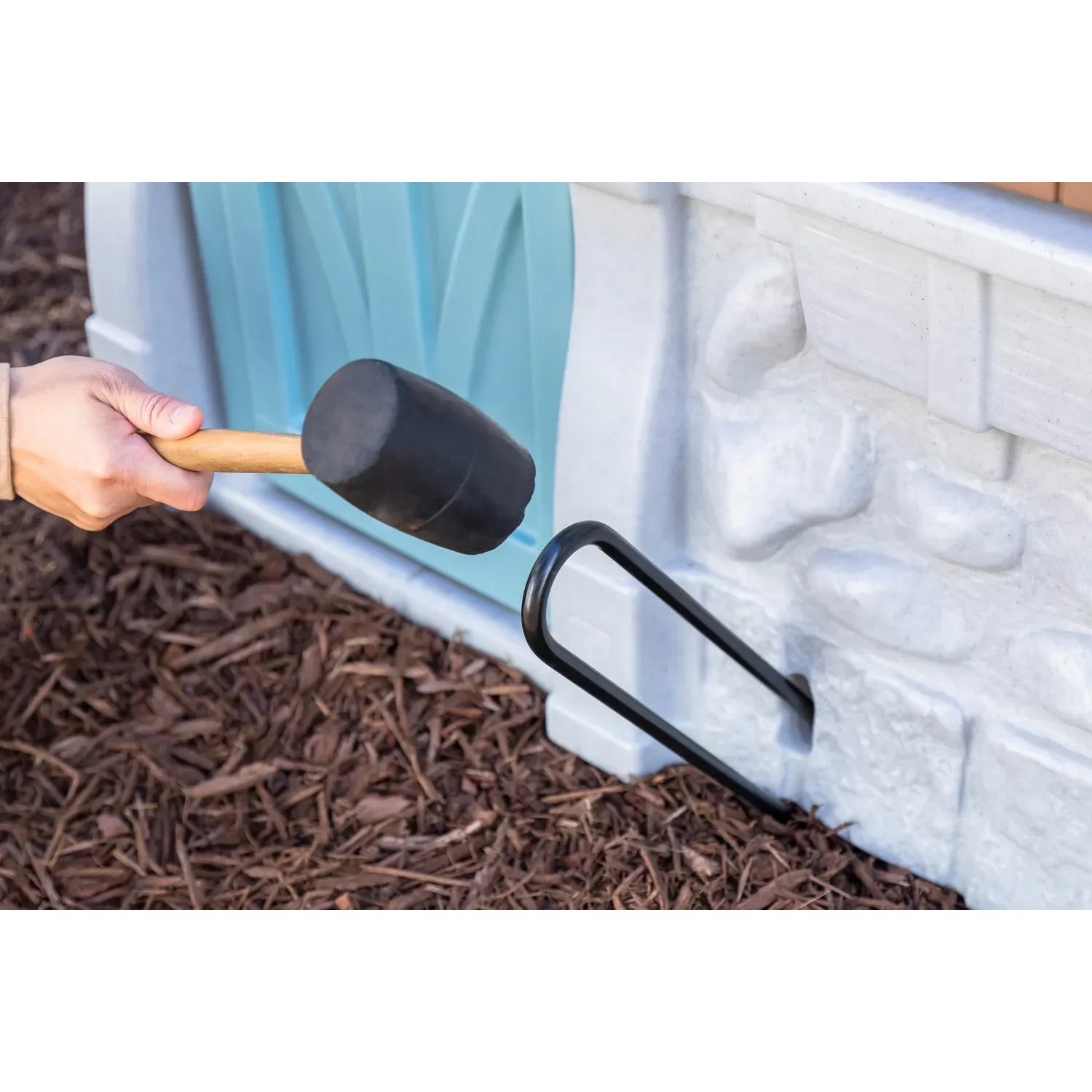 Aufbau des Step2 Spielhaus Adventures: Gummihammer fixiert Hering am Spielhaus.