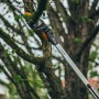 Fiskars Teleskop-Schneidgiraffe UPX86 beim Schneiden eines Astes. Gartenschere mit langem, silberfarbenem Stiel.