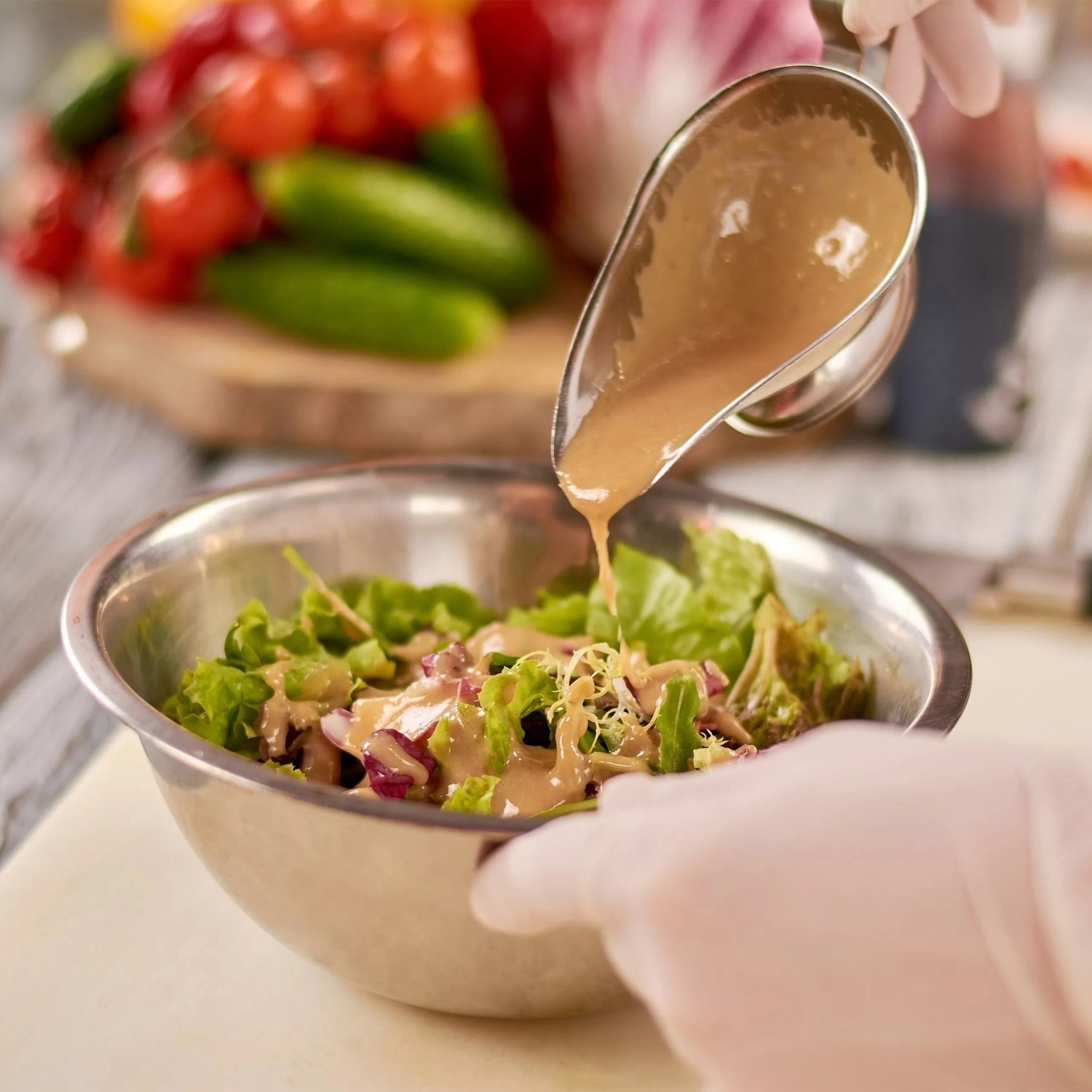 Silberne Edelstahl Rührschüssel mit frischem Salat, Dressing wird eingegossen. Vielseitiger Küchenhelfer.