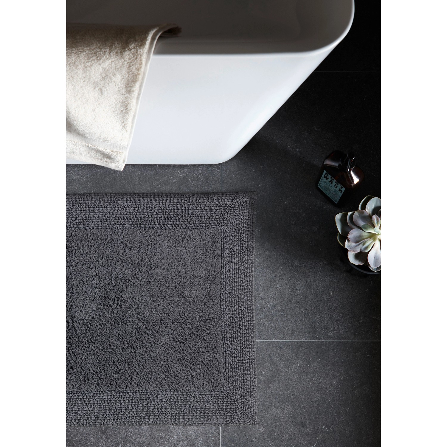 Schöner Wohnen Badteppich Bahamas, 67x110 cm, anthrazit, vor Badewanne auf dunklen Fliesen.