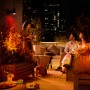Philips Hue Lily Spot Basis-Set: 3-flammige LED-Gartenleuchte in Schwarz illuminiert eine Dachterrasse mit Personen.