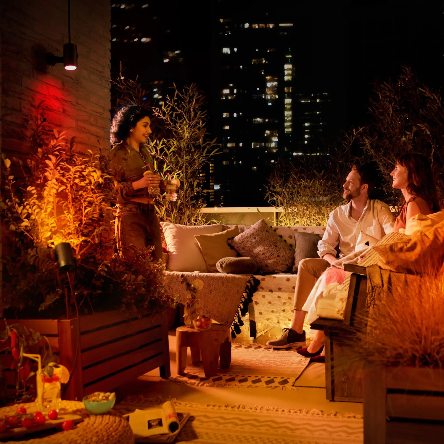 Philips Hue Lily Spot Basis-Set: 3-flammige LED-Gartenleuchte in Schwarz illuminiert eine Dachterrasse mit Personen.