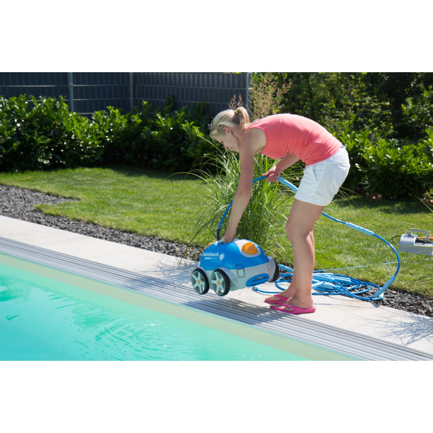 Frau bedient Steinbach Speedcleaner Poolrunner am Pool. Automatischer Poolsauger in Blau und Weiß.