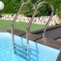 Edelstahltreppe im Gre Echtholzpool Canelle 2, oval, mit brauner Holzumrandung und blauem Wasser.