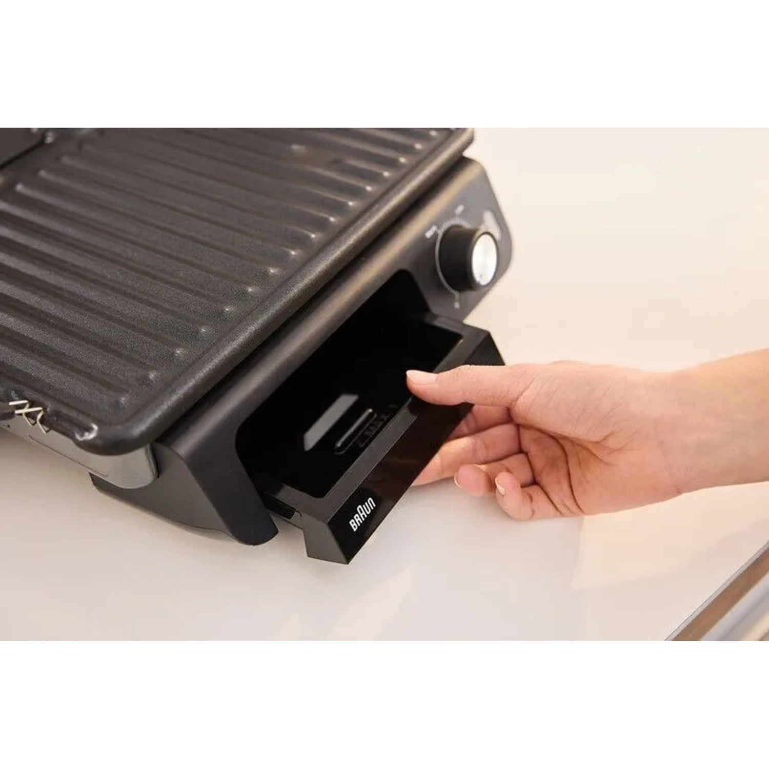 Grauer Braun Multigrill mit Fettauffangschale in der Hand.
