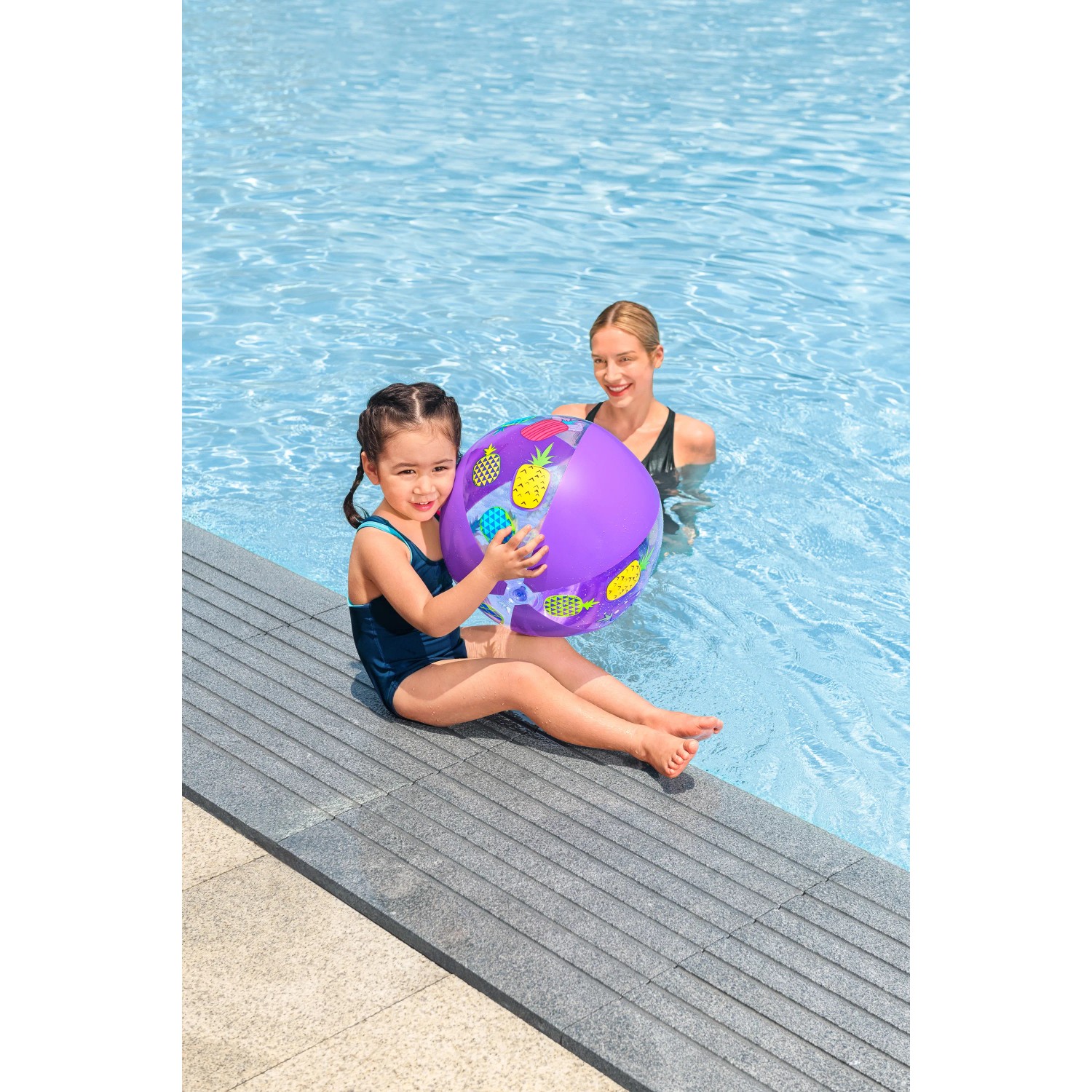 Mädchen mit lila Bestway Wasserball mit Ananas-Motiv am Pool, Mutter im Hintergrund.