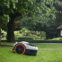 Grauer Segway Navimow i105E Mähroboter ohne Kabel auf Rasen vor Garten.