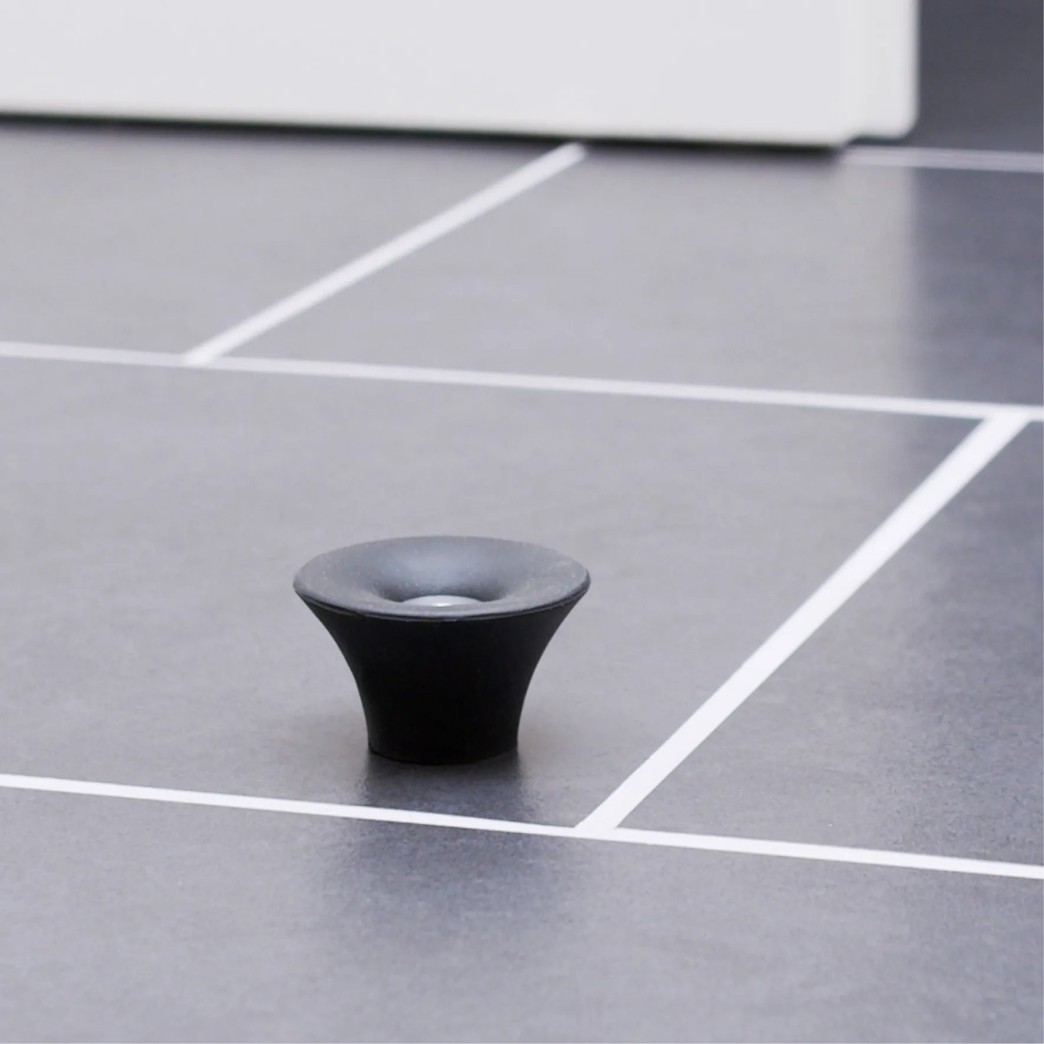 Schwarzer Wagner Bodentürstopper EH5202 aus Gummi zum Schrauben auf grauem Boden.