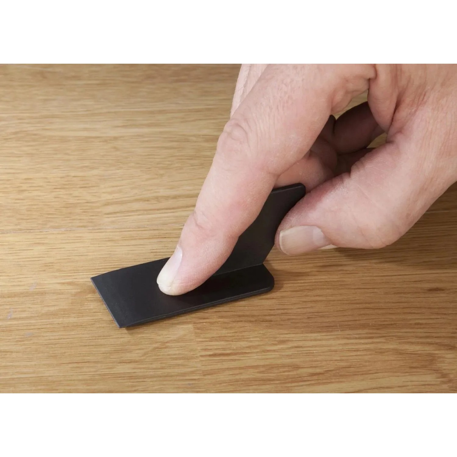 Hand glättet mit schwarzem Spachtel eine Ausbesserung auf hellem Laminat oder Parkett. Westfalia Reparatur-Set.