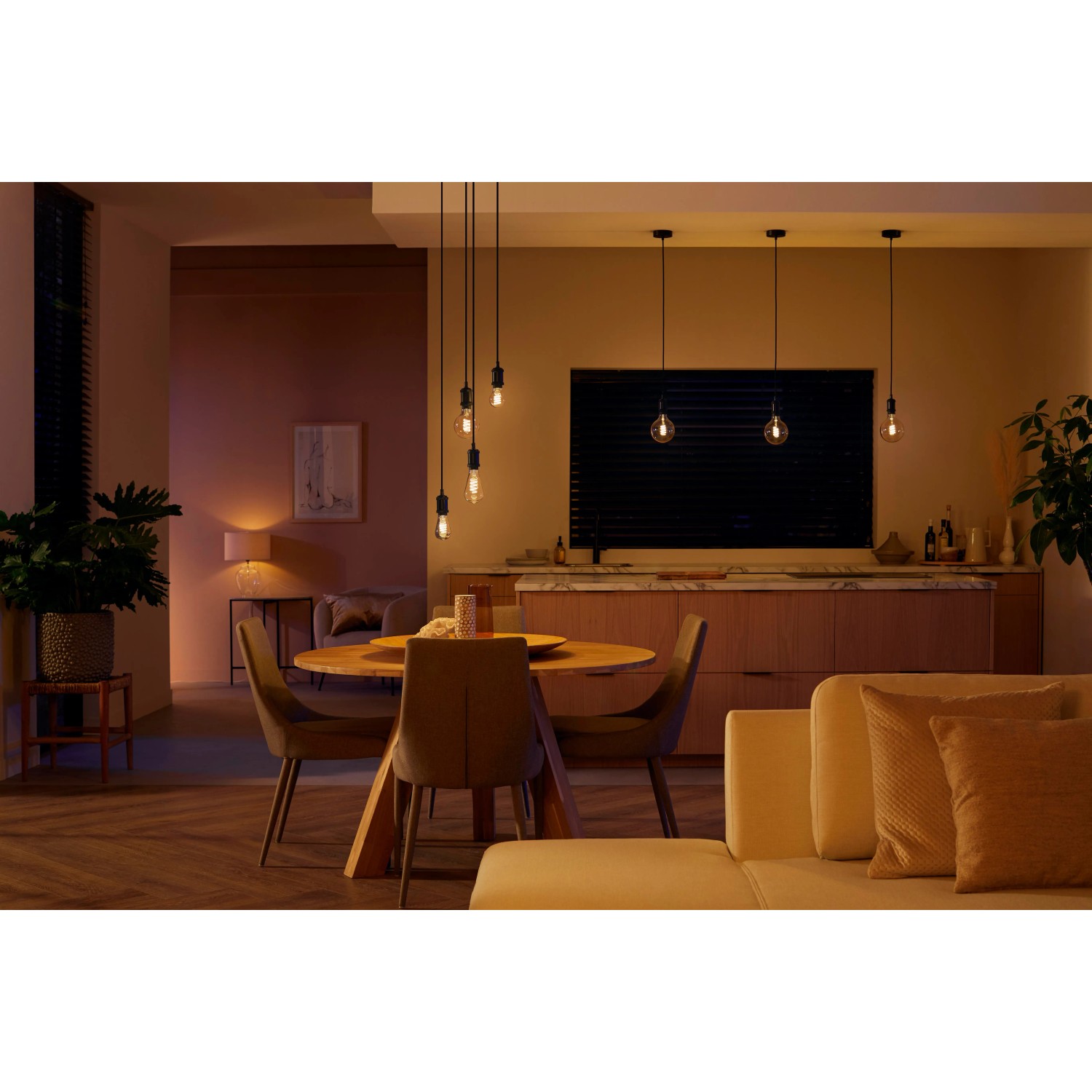 Philips Hue Filament Lampe E27 in Wohnraum-Szene mit Esstisch und Sofa.
