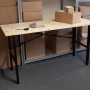 rikta Werkbank (159x85x58cm) mit Holzplatte und schwarzem Stahlgestell vor Regalen mit Kartons.