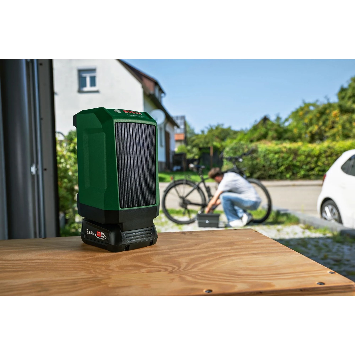 Grüner Bosch UniversalSpeaker 18V-1 Akku-Bluetooth-Box auf Holztisch, mit 18V Akku, im Freien bei Fahrradreparatur.