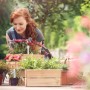 Frau mit roten Haaren bepflanzt Garten, nutzt weiße Kunststoff Stecketiketten für Blumen und Kräuter in Holzkisten.
