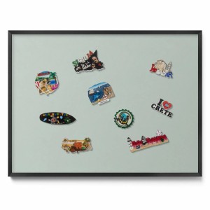 Bedruckte, hellgrüne Magnettafel (80x60 cm) mit schwarzem Rahmen und Reisesouvenir-Magneten.