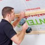 Mann befestigt Rockwool Formrock Untersparrendämmung (60mm) mit einem Akkuschrauber an einer Holzkonstruktion.