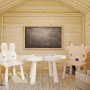 Gemütliches Palmako Toby Holzspielhaus innen mit Kindertisch, Hasen- und Hirschstuhl. Eine Tafel hängt an der hellen Holzwand.