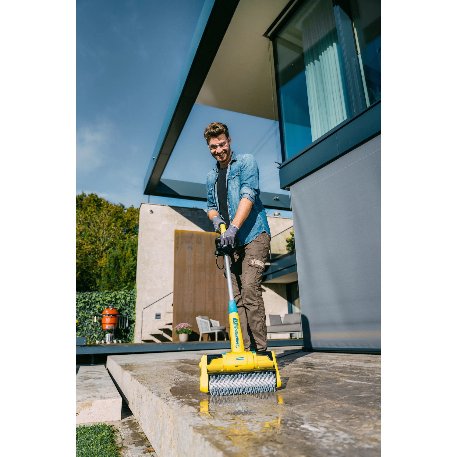 Mann reinigt Terrasse mit Gloria MultiBrush XL Elektro-Oberflächenbürste. Gartenhandgerät mit XL-Arbeitsbreite.