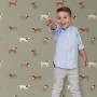 ESTAhome Vliestapete mit braunen Hunden auf grünem Grund im Kinderzimmer, ein Kind zeigt lachend auf das Muster.