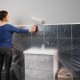 Frau streicht Wand mit Tesa Abdeckfolie Easy Cover Economy L. Schutz vor Farbspritzern.