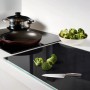 Schwarze Glas Herdabdeckplatte (80x52 cm) mit Brokkoli und Messer auf einer Küchentheke.
