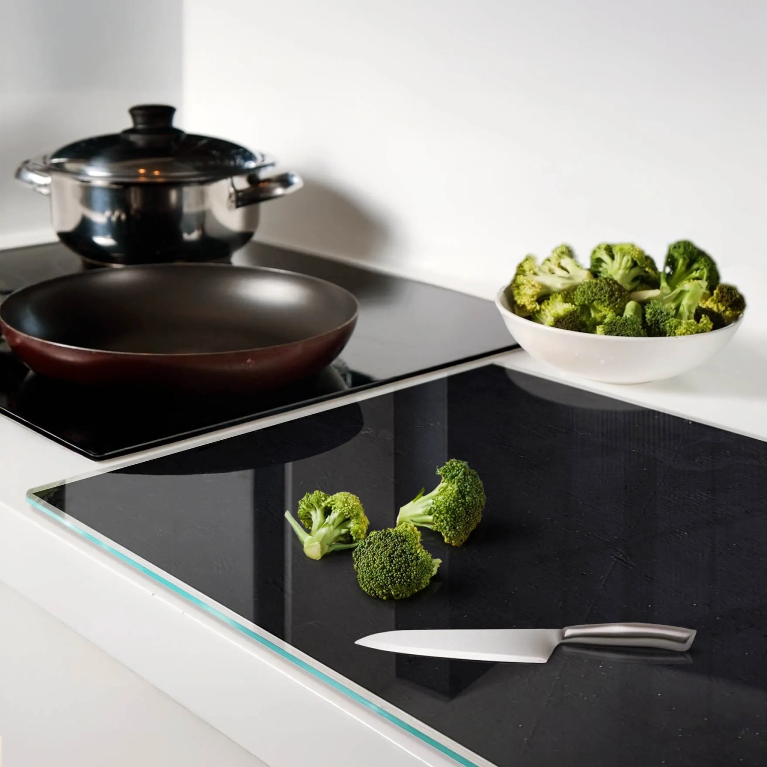 Schwarze Glas Herdabdeckplatte (80x52 cm) mit Brokkoli und Messer auf einer Küchentheke.