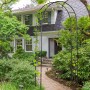 Schwarzer Outsunny Rosenbogen aus Metall mit Spitze im Garten, teilweise mit Ranken bewachsen.